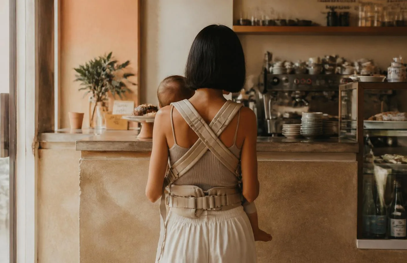 Vassiliki mit ihrem Sohn in der Trage am Tresen eines Cafés, von hinten fotografiert